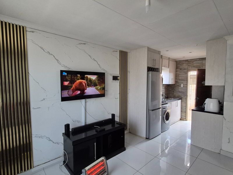 Modern open-plan living area featuring marble-effect wall cladding, gold slat accents, and a compact, functional kitchen with tiled flooring throughout.