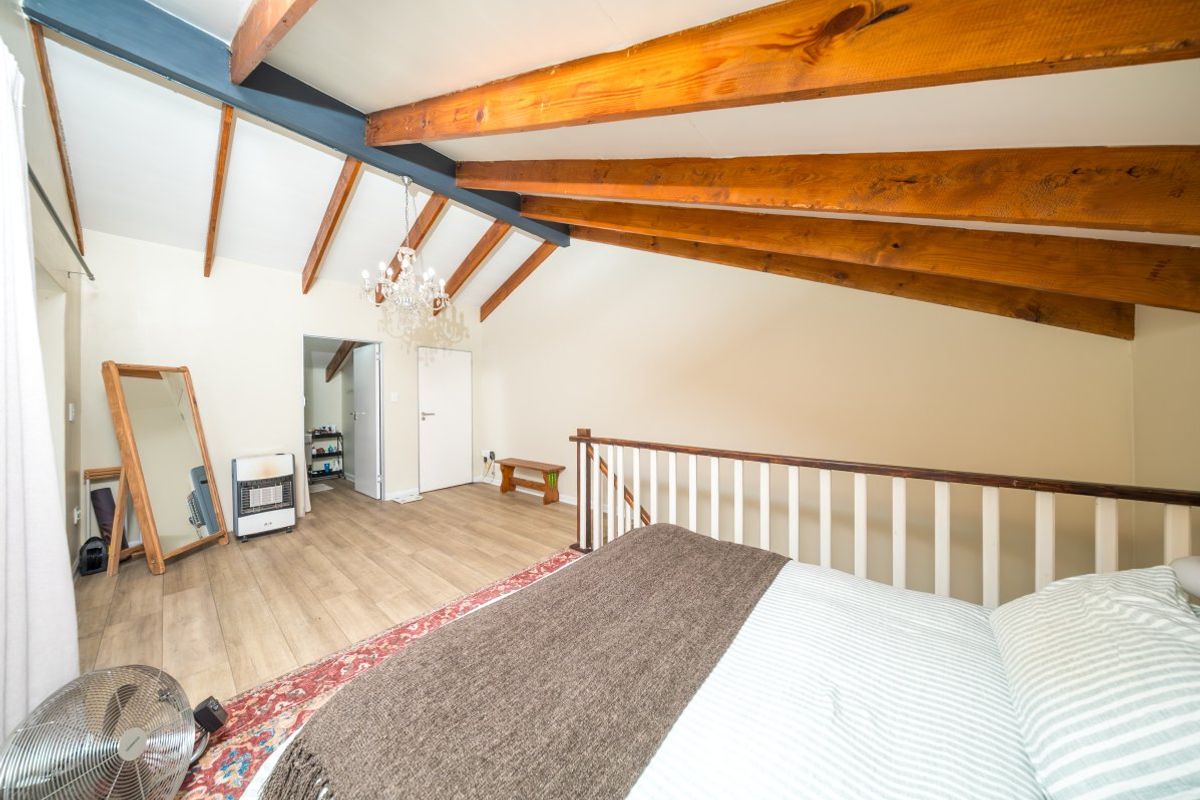 A loft-style bedroom featuring exposed timber ceiling beams, laminate flooring, and a timber balustrade overlooking the lower level.