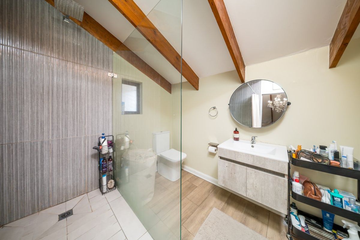 Modern bathroom featuring a walk-in shower with glass screen, vanity unit with basin, toilet, and exposed timber ceiling beams.