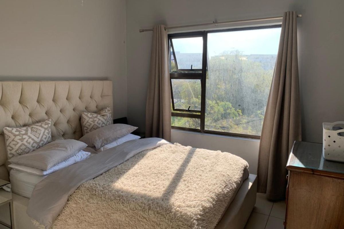 A bedroom featuring tiled flooring and a large aluminium-framed window providing natural light and exterior views.