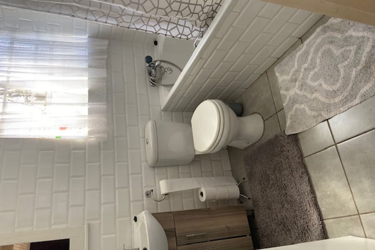 A clean, functional bathroom featuring white subway tile wall cladding, a vanity cabinet with basin, a toilet, and a bathtub with shower mixer.