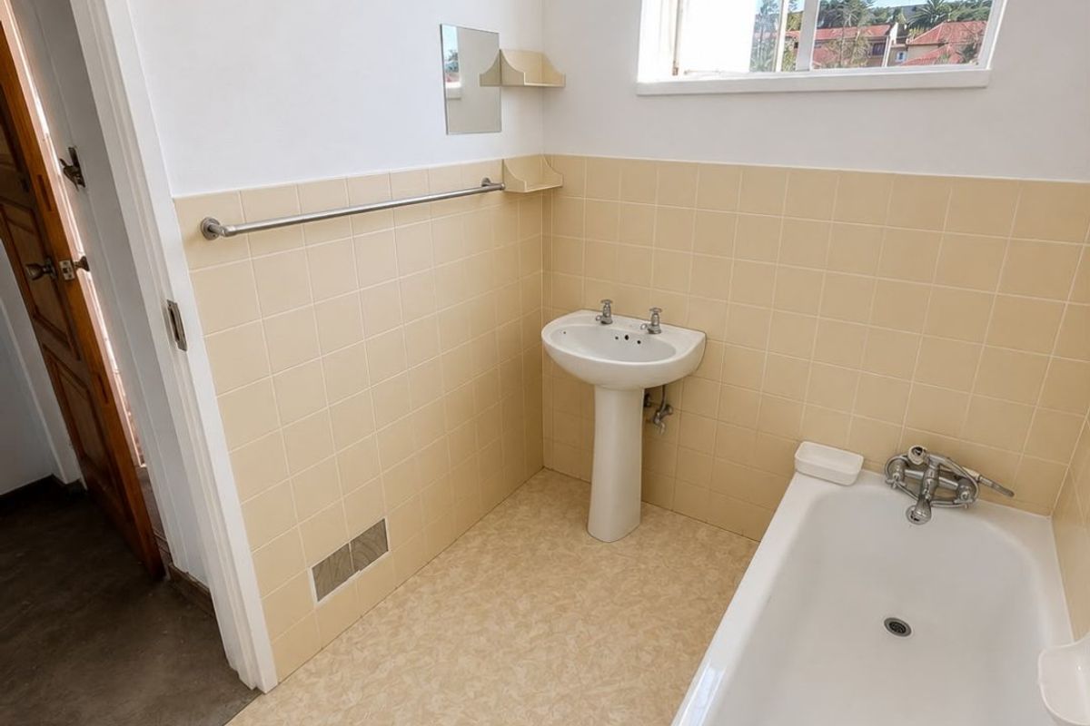 A functional bathroom featuring a pedestal basin, bathtub, and tiled splashbacks, offering a clean, dated aesthetic ready for modernization.