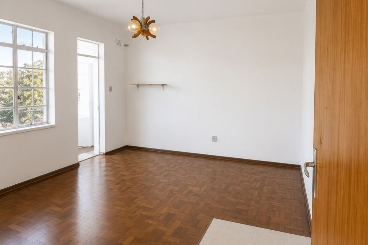 A bright, empty living room featuring classic parquet flooring, a tiled entryway, and a large window providing natural light.