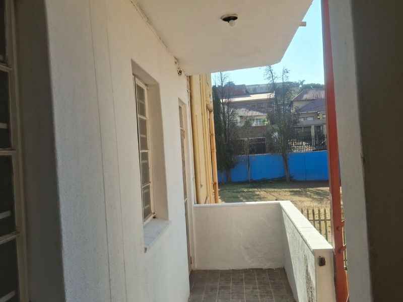 A covered balcony area featuring tiled flooring and a concrete balustrade, offering an outdoor space with views of the surrounding neighborhood.