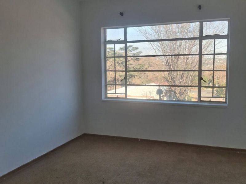 An empty bedroom featuring a large steel-framed window with neighborhood views and carpeted flooring, ready for renovation or staging.