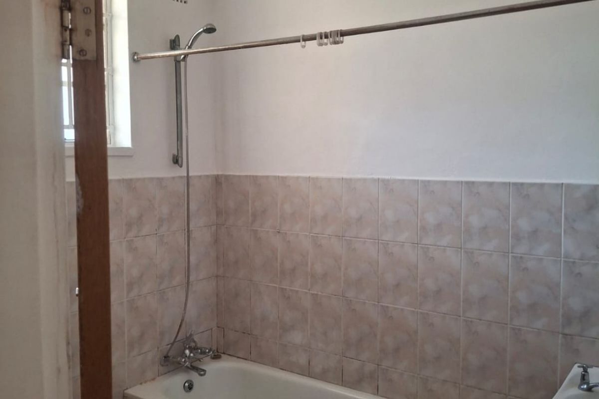 A functional bathroom featuring a bathtub with shower mixer, tiled walls and flooring, and a basin, requiring some cosmetic updates.