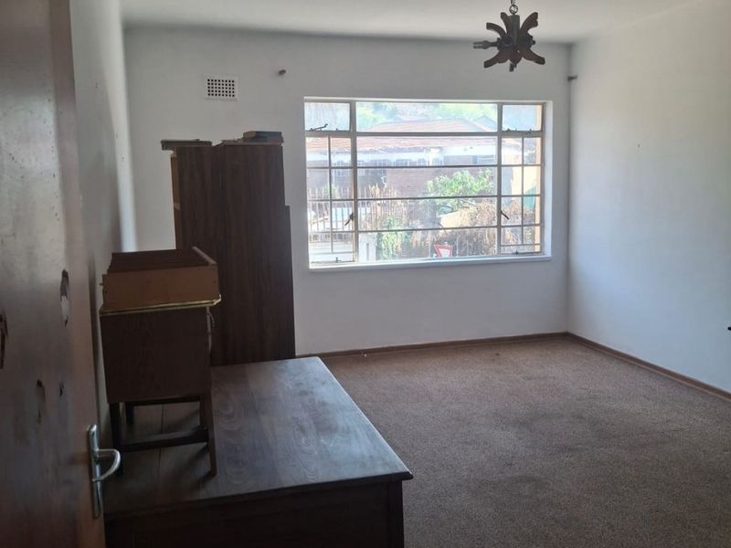 A bedroom featuring carpeted flooring, a steel-framed window, and a ventilation grille. The room requires cosmetic updates to improve its overall condition.