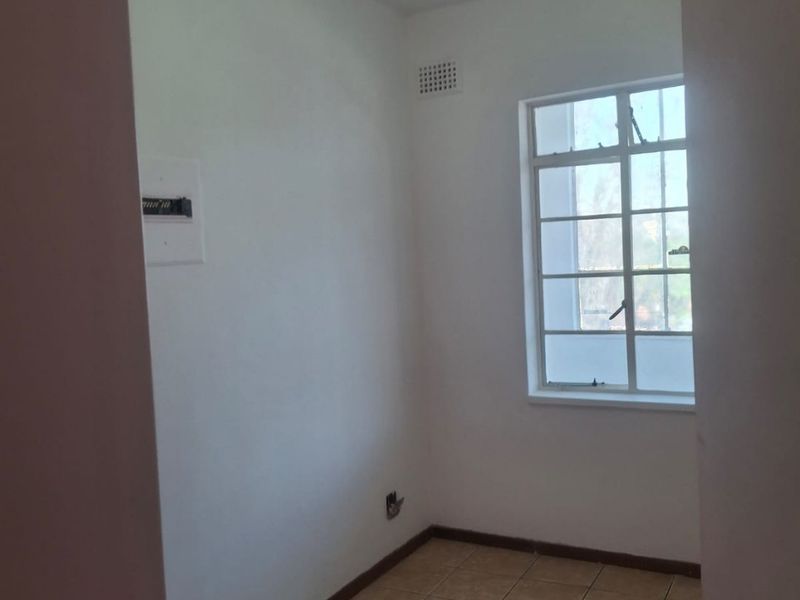 A compact, empty bedroom featuring tiled flooring, a window with security bars, and a ceiling light fixture.