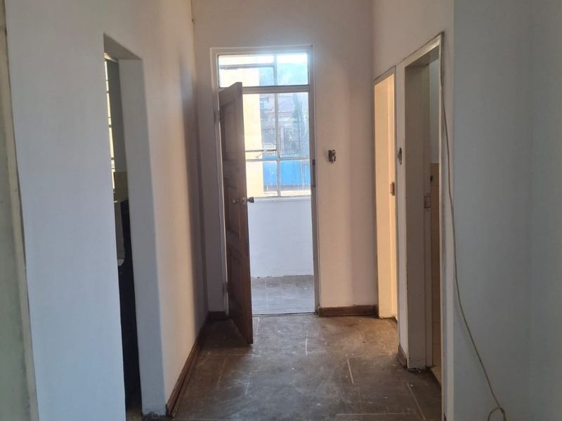 A vacant hallway featuring plain walls, internal door frames, and exposed flooring, leading to an exterior doorway.