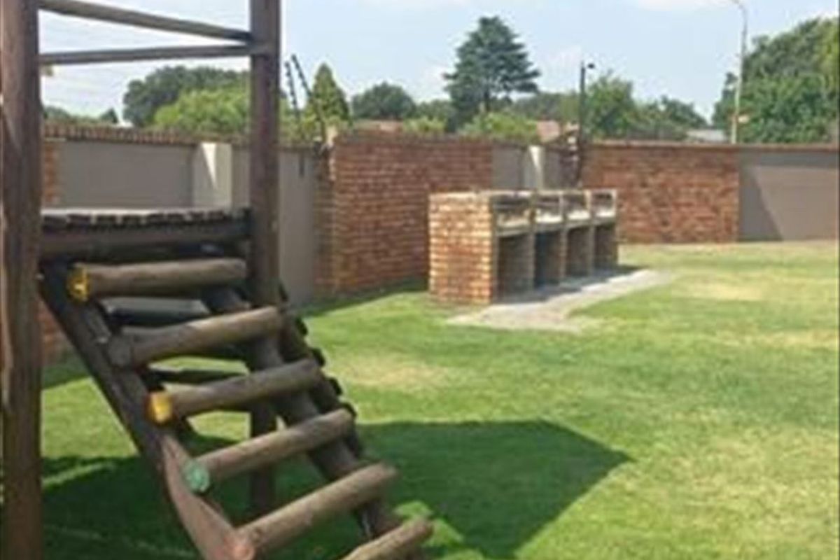 Spacious garden area featuring a built-in brick braai, enclosed by a secure brick boundary wall with electric fencing.