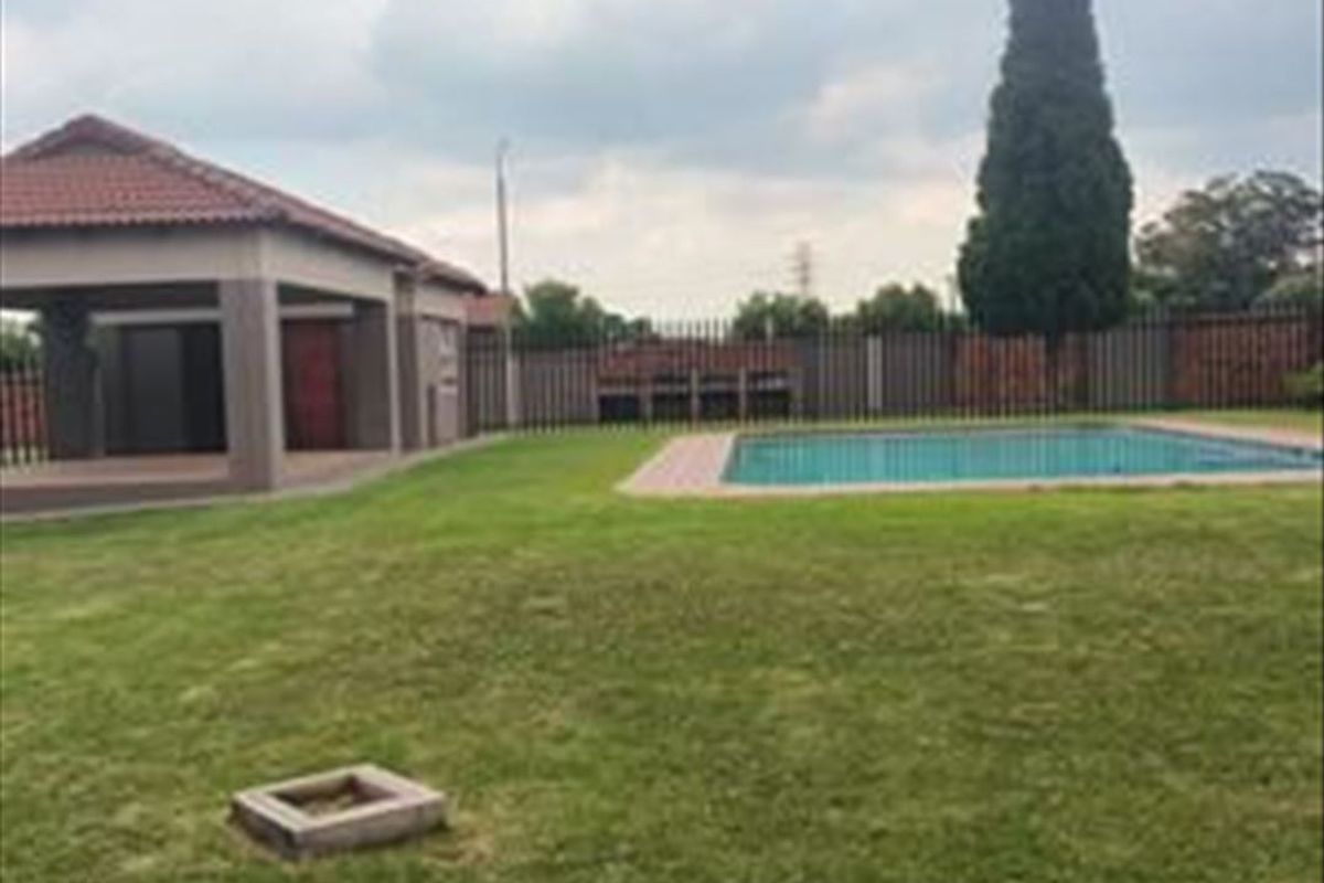 Spacious backyard featuring a swimming pool, a covered patio area, and well-maintained lawn, enclosed by perimeter fencing.