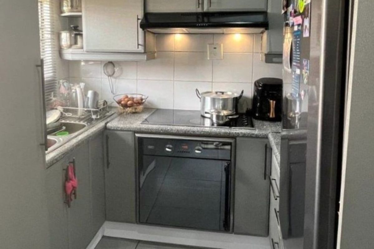 Compact, functional kitchen featuring grey cabinetry, granite countertops, tiled backsplash, and integrated appliances including an oven, hob, and extractor fan.