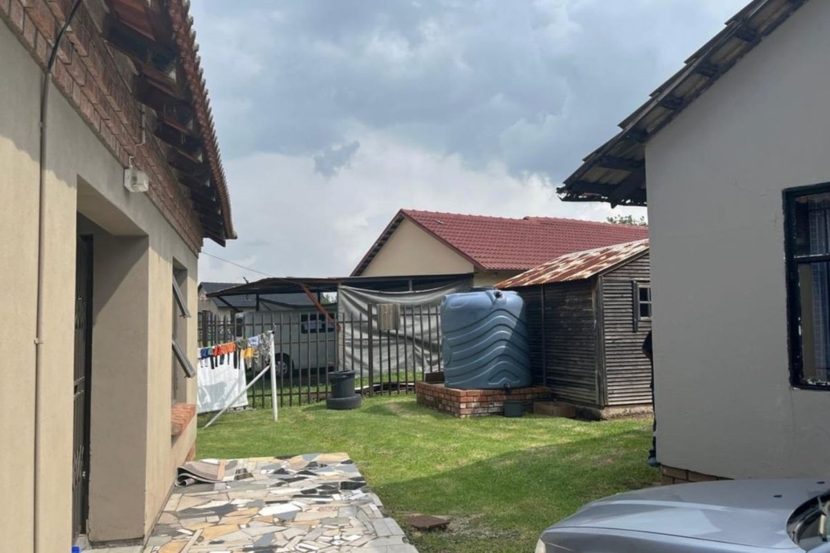 Rear yard area featuring a lawn, paved walkway, water storage tank on a brick base, and a small storage shed with a rusted roof.
