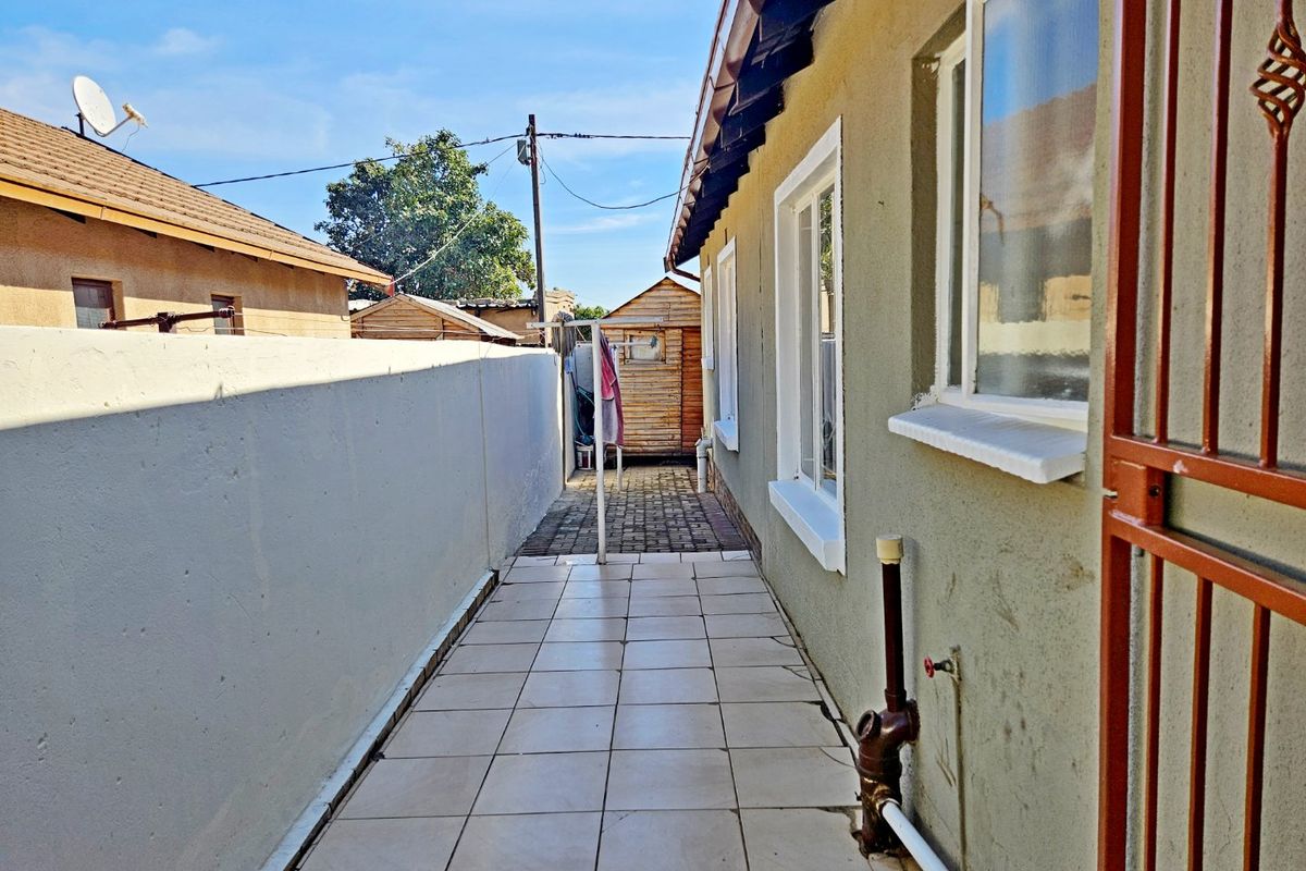 A narrow side passage featuring tiled flooring, a boundary wall, and external plumbing fixtures along the side of the house.