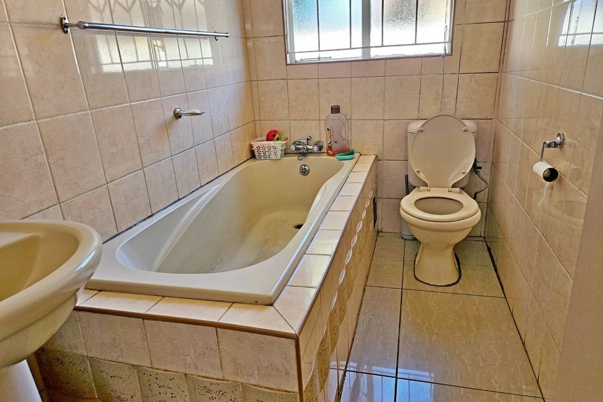A dated bathroom featuring a built-in bathtub, pedestal basin, and toilet, finished with neutral ceramic wall and floor tiles.