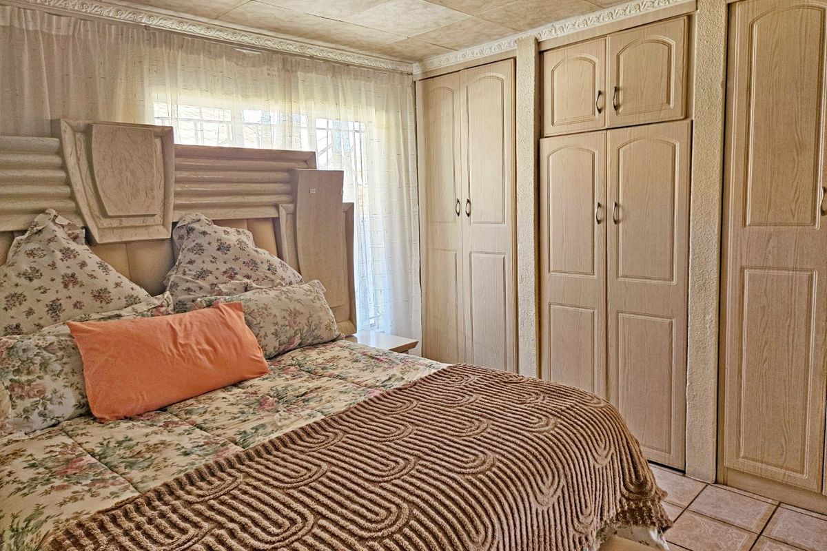 A bedroom featuring built-in wooden cupboards, tiled flooring, and decorative ceiling tiles, offering a functional space with potential for modern updates.