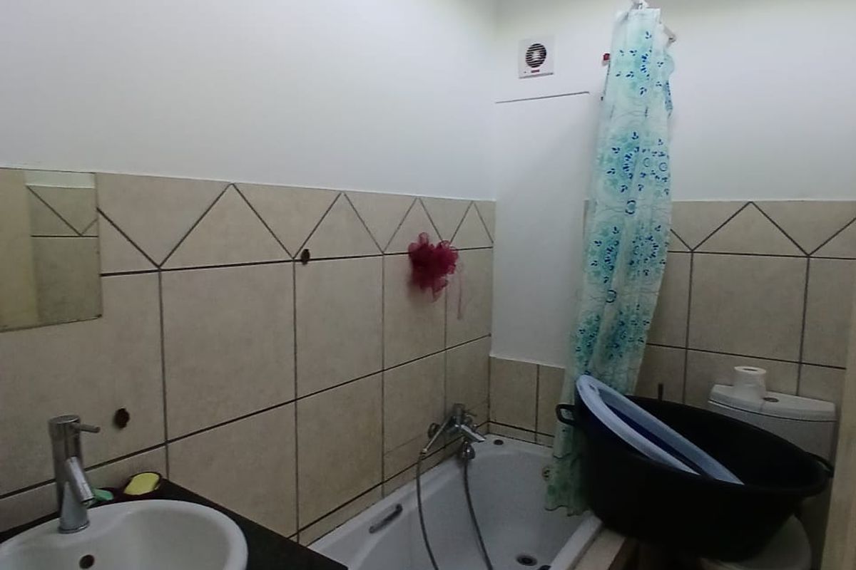 A functional bathroom featuring a vanity with basin, a bathtub with shower attachment, and a toilet, finished with neutral wall and floor tiling.