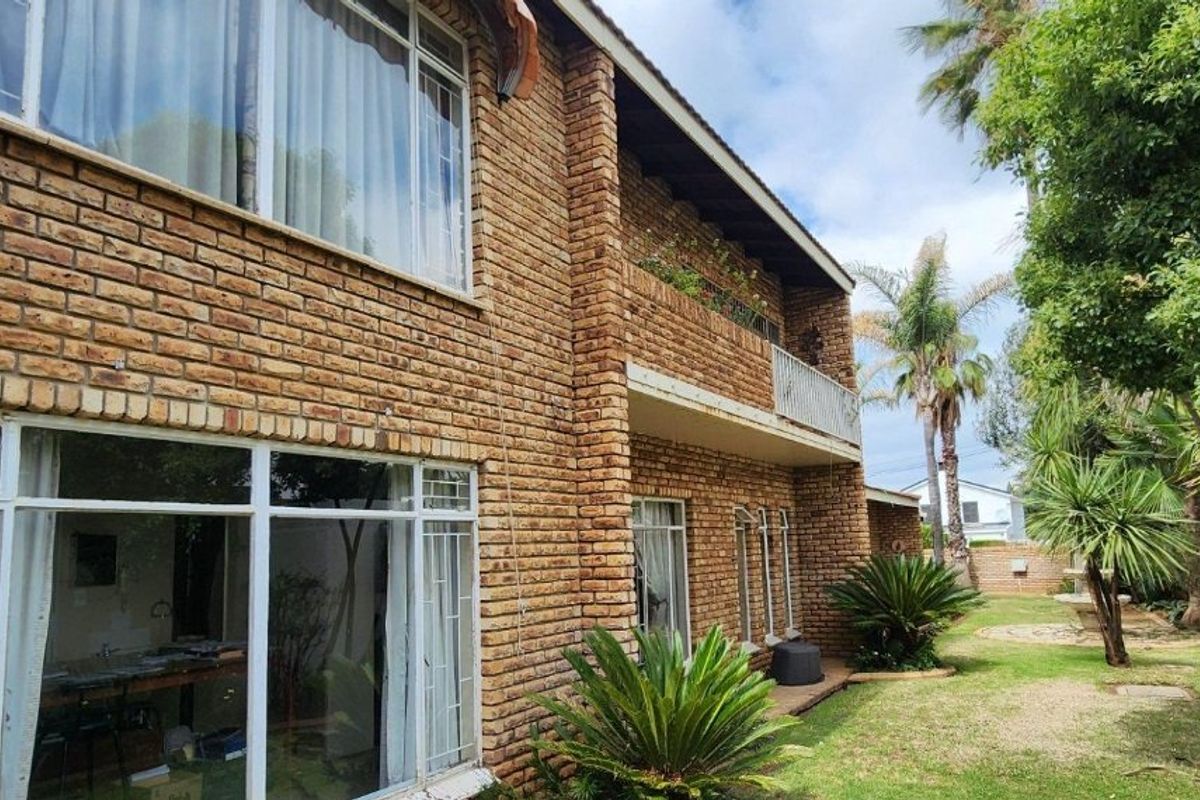Rear view of a double-storey face brick house featuring a balcony, large windows with security bars, and a well-maintained garden area.