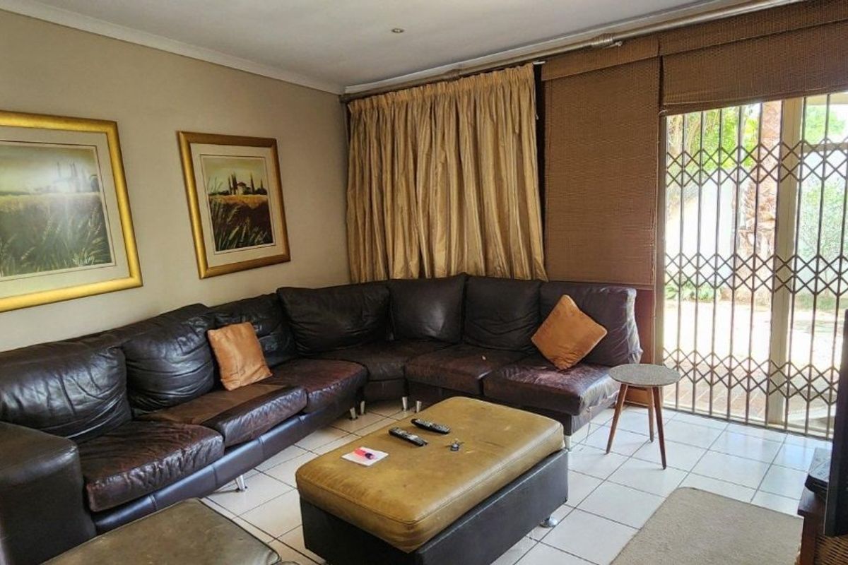 A comfortable living room featuring tiled flooring and a sliding glass door with security gate, providing direct access to the outdoor area.