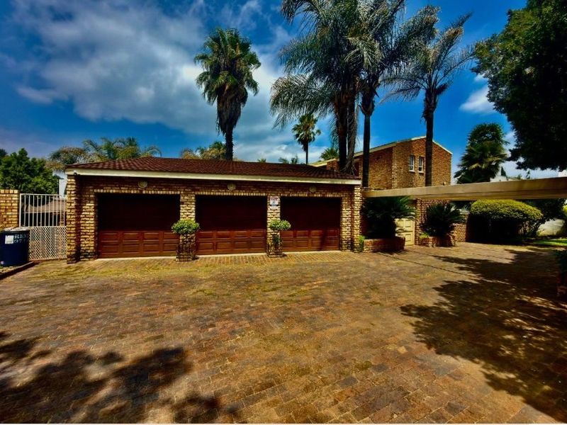 Front exterior view of a property featuring a triple garage, brick paved driveway, and an attached carport.