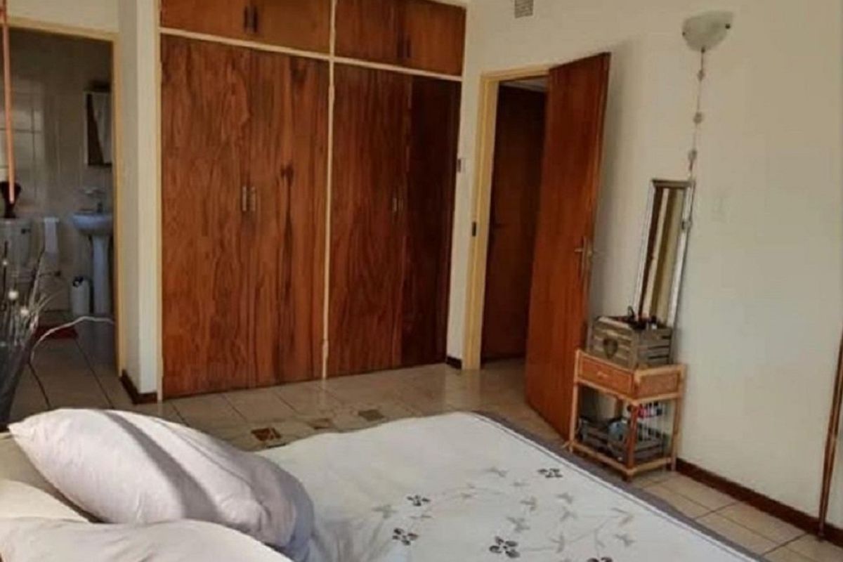 A bedroom featuring built-in wooden cupboards and tiled flooring, with an adjacent view into a bathroom area.