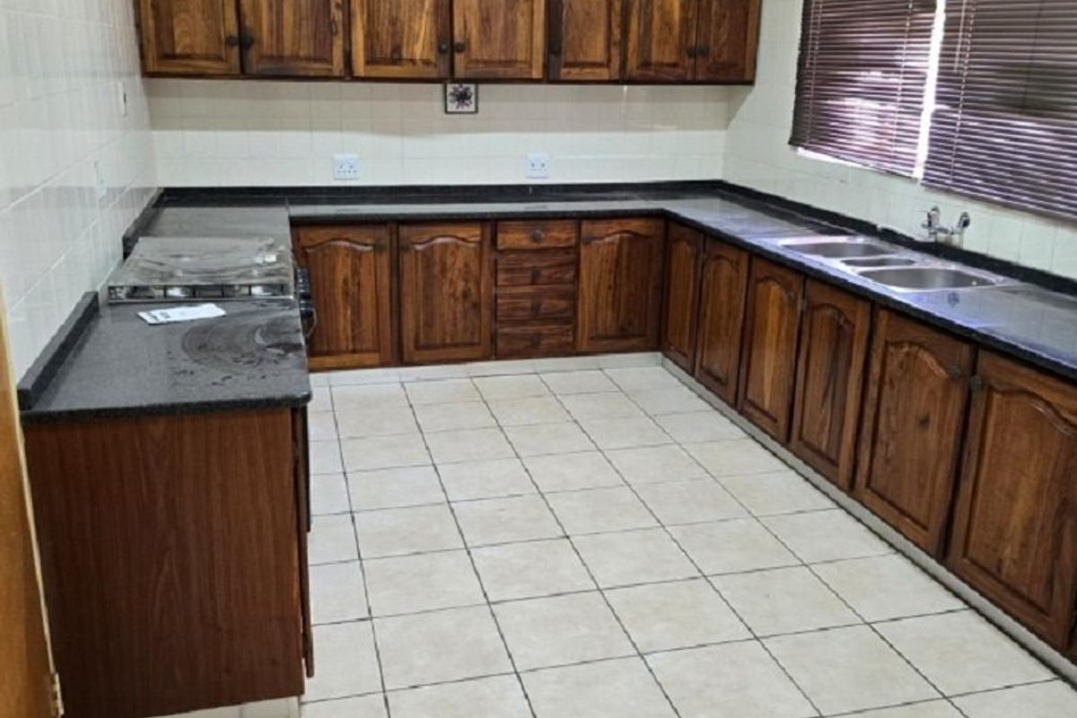 A functional kitchen featuring wooden cabinetry, granite countertops, a double basin sink, and tiled flooring. The space is well-lit and ready for modernization.