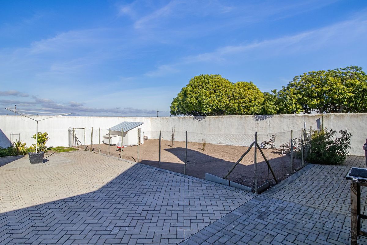 A spacious rear yard featuring extensive paving, a perimeter wall, and a dedicated enclosed area, offering potential for landscaping or outdoor development.