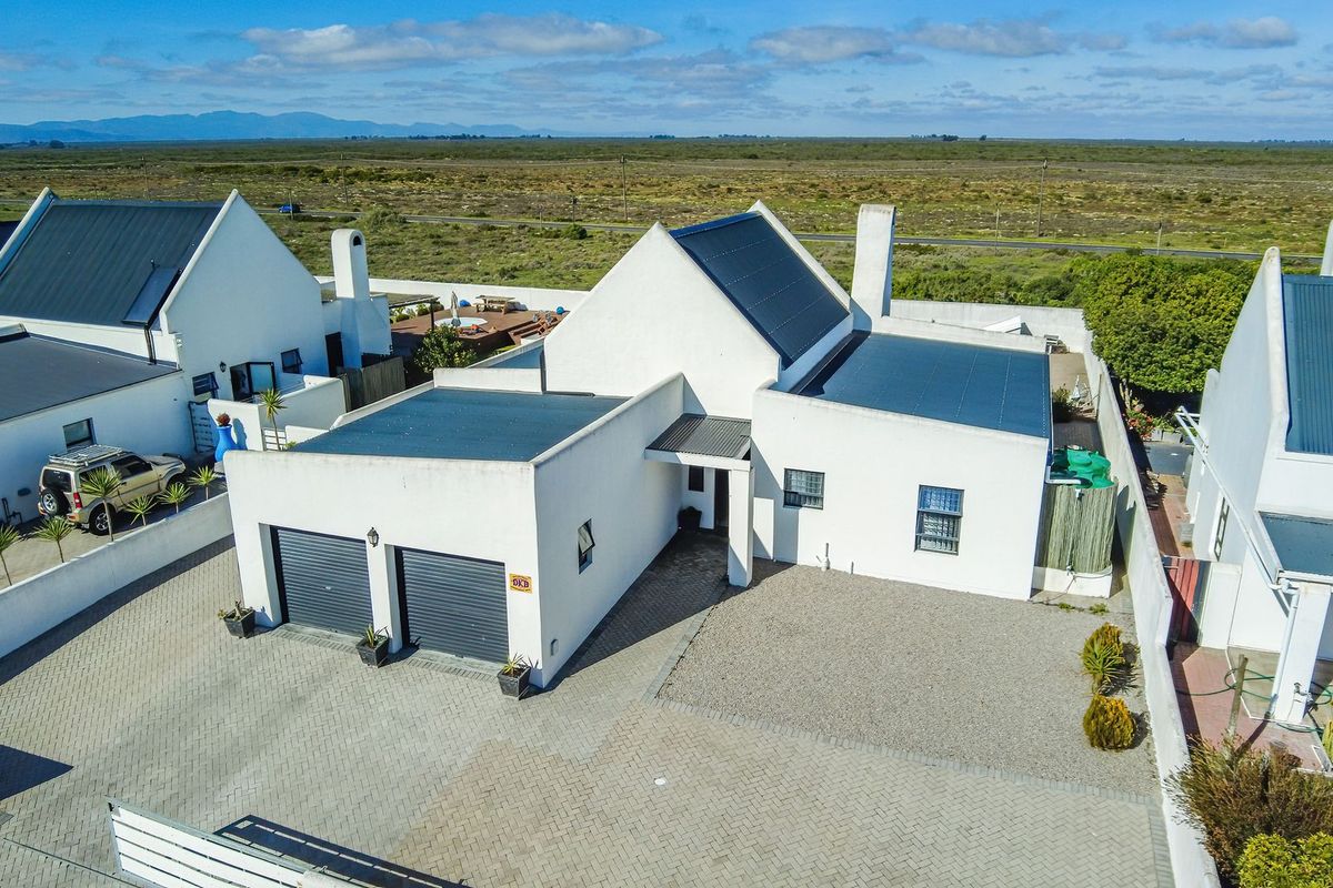 Aerial view of a modern white house featuring a double garage, paved driveway, and metal roofing in a coastal estate setting.