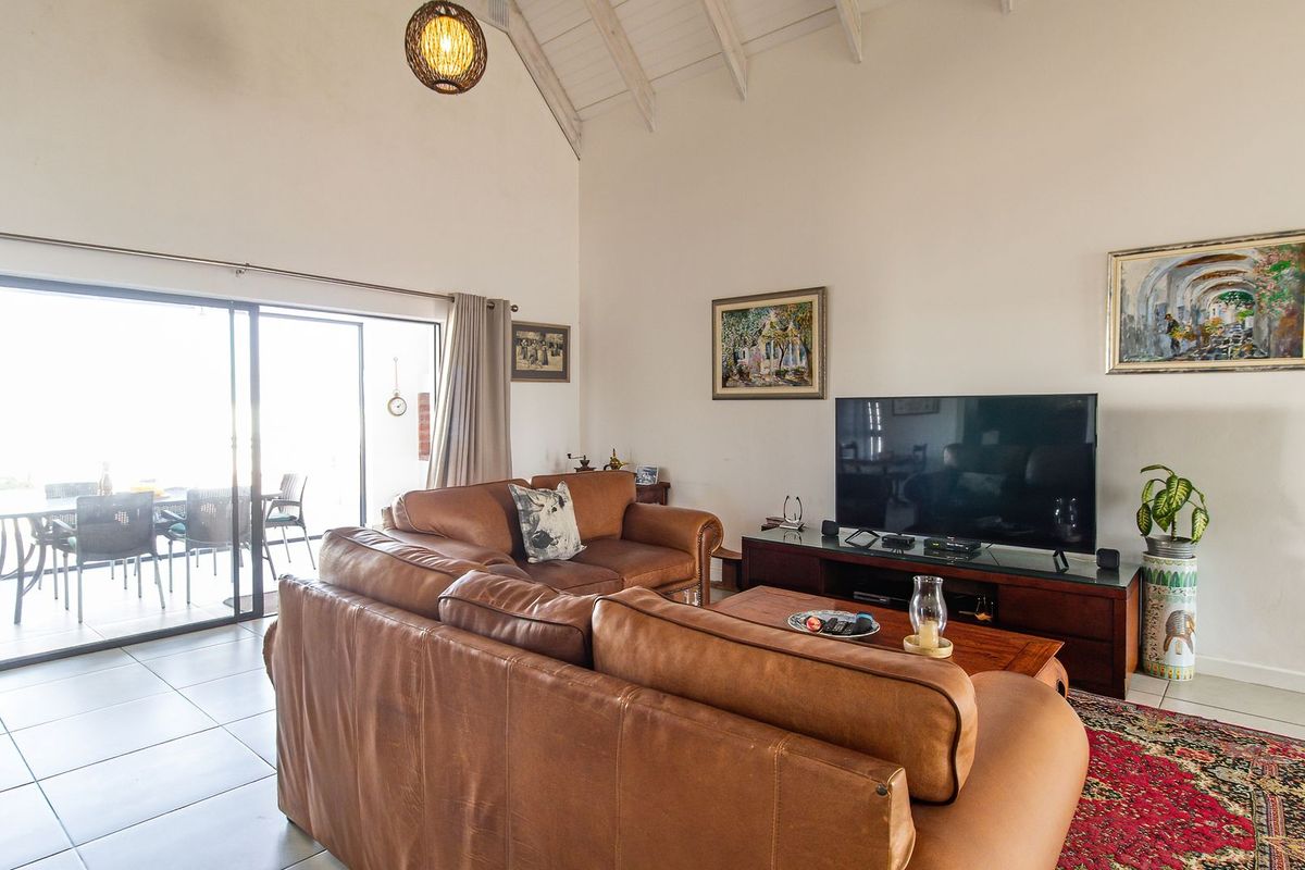 Spacious living room featuring high vaulted ceilings with exposed rafters, tiled flooring, and large sliding glass doors providing access to the outdoor patio area.