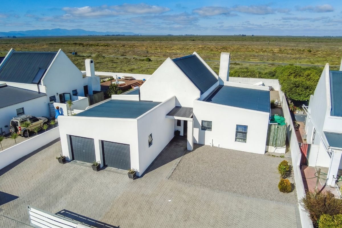 Aerial view of a modern residential property featuring a double garage, paved driveway, and metal roofing in a coastal estate setting.