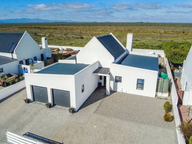 Aerial view of a modern residential property featuring a double garage, paved driveway, and metal roofing in a coastal estate setting.