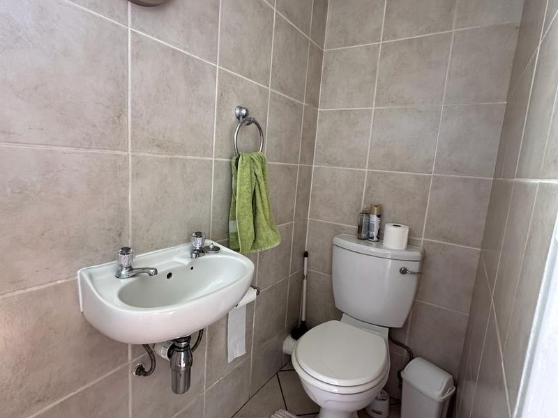 A compact guest bathroom featuring neutral ceramic wall and floor tiling, a wall-mounted basin, and a standard toilet.