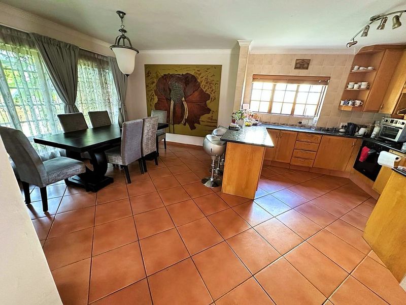Open-plan kitchen and dining area featuring wooden cabinetry, granite countertops, built-in appliances, and terracotta-style tiled flooring.