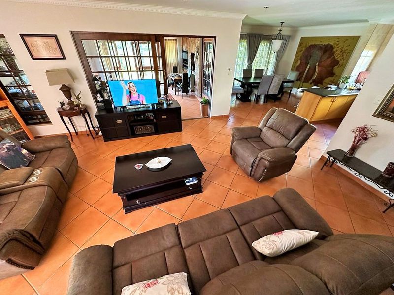 Spacious open-plan living and dining area featuring terracotta floor tiles, wooden framed glass doors, and a functional kitchen island layout.