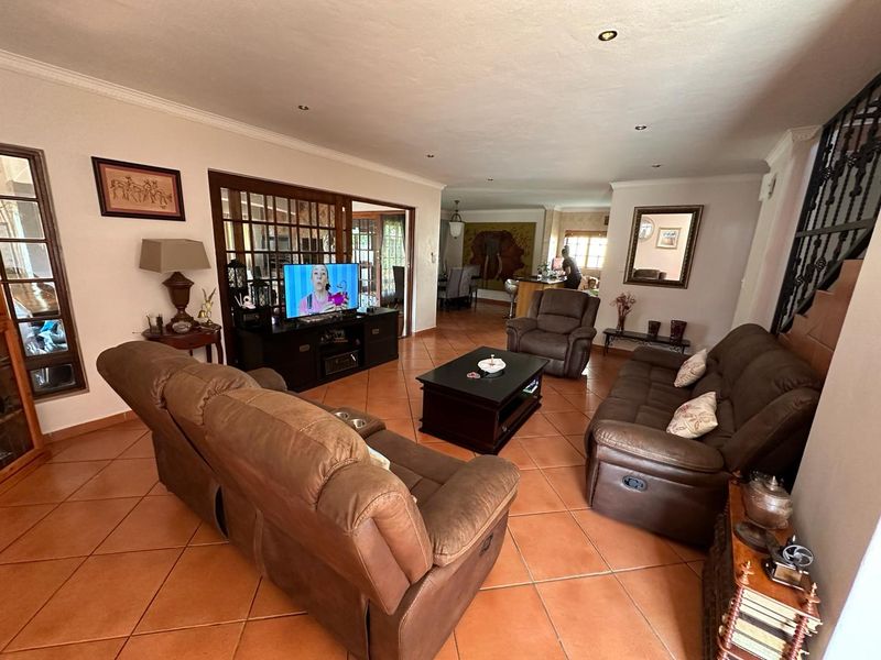 Spacious open-plan living area featuring terracotta floor tiles, recessed lighting, and a wrought iron staircase, connecting seamlessly to the adjacent dining and kitchen space.