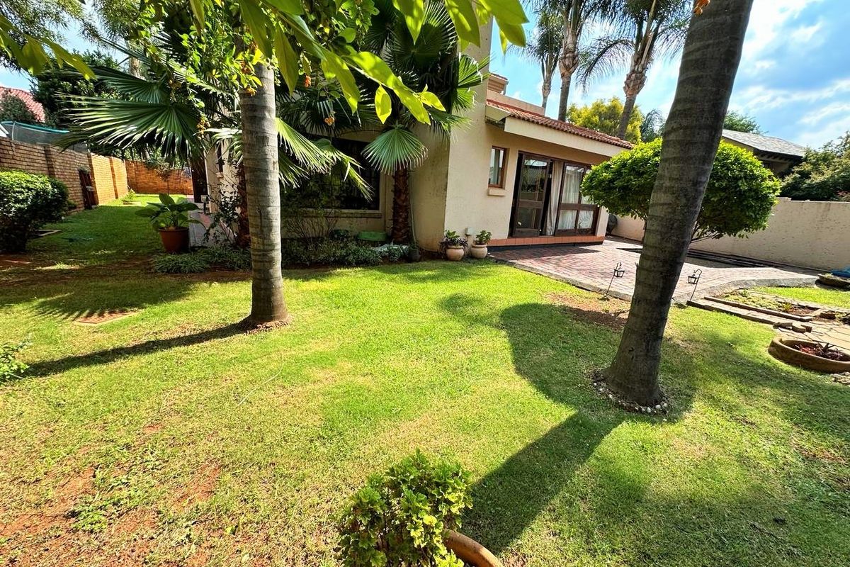 A well-maintained rear garden featuring a paved patio area, established palm trees, and a brick boundary wall, offering a private outdoor space.