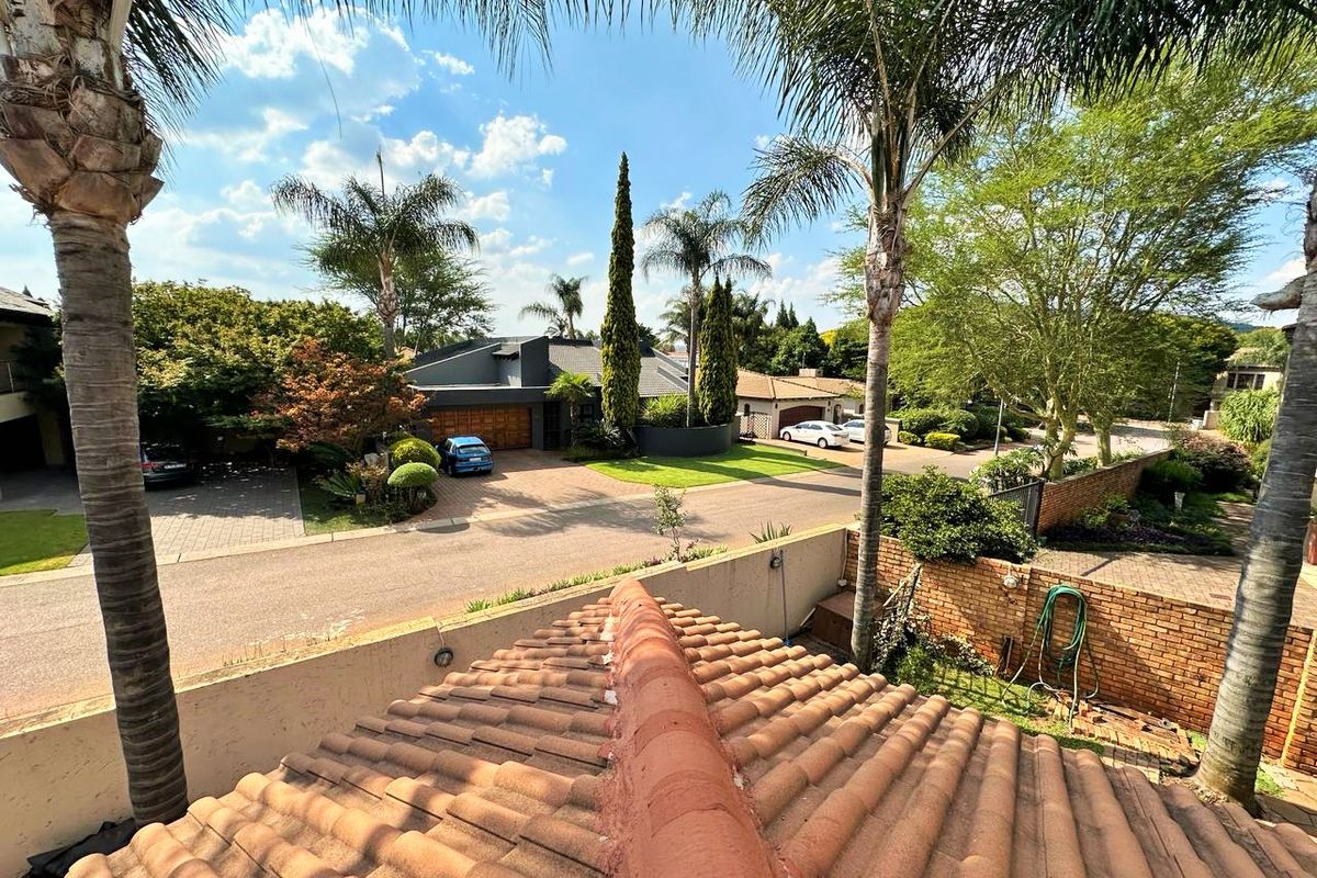 An elevated aerial view showing the property's tiled roof, surrounding brick boundary walls, paved driveway, and established garden landscaping within the residential estate.