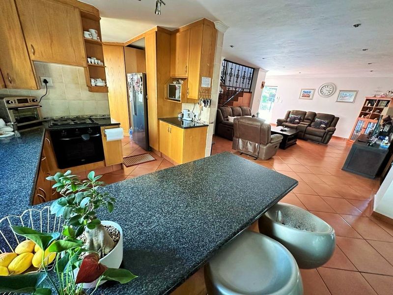 Spacious open-plan kitchen and living area featuring granite countertops, wooden cabinetry, built-in appliances, and tiled flooring throughout.