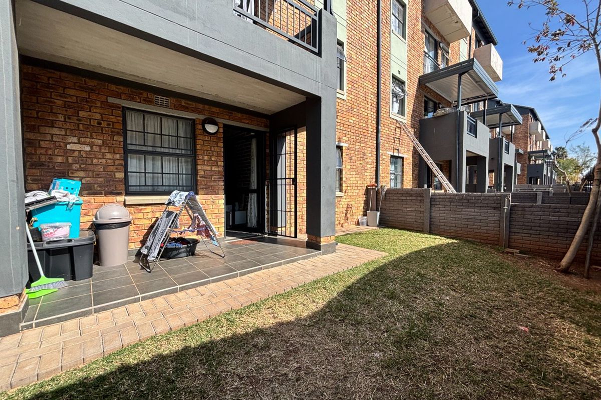 Rear view of the apartment building featuring a private tiled patio area and a small garden space with brick boundary walling.