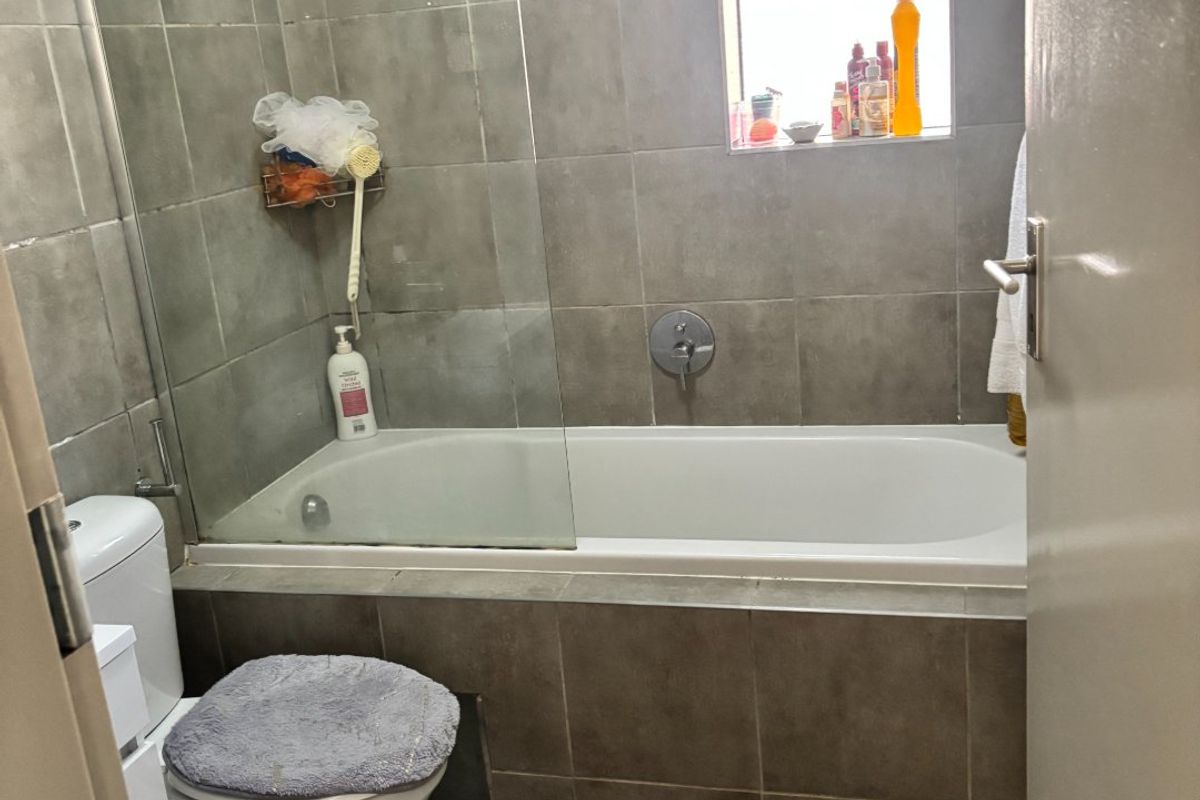 A functional bathroom featuring a built-in bathtub with a glass shower screen, tiled walls, and a standard toilet.