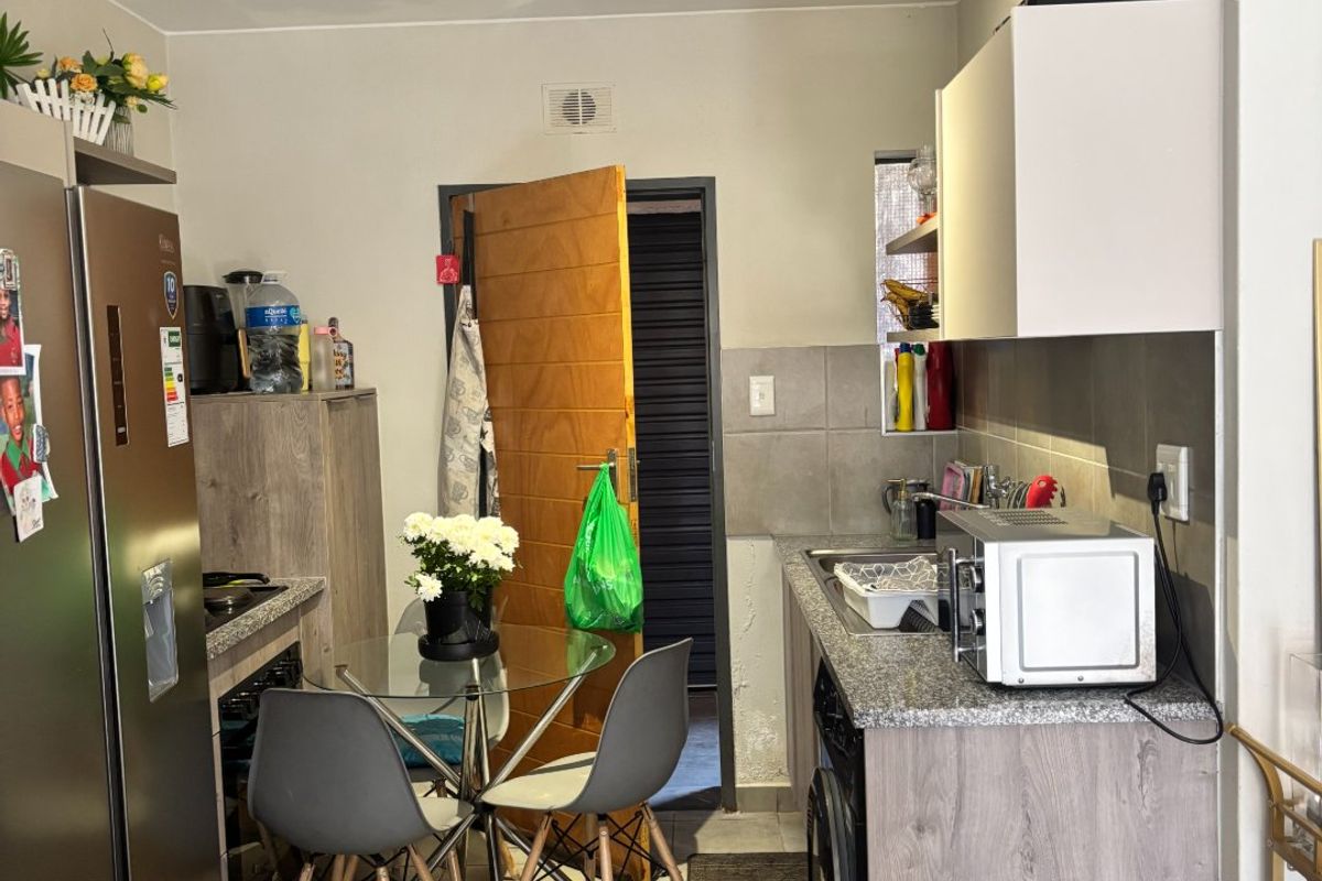 Compact kitchen featuring modern grey cabinetry, granite countertops, tiled backsplash, and tiled flooring, with direct access to an external area.