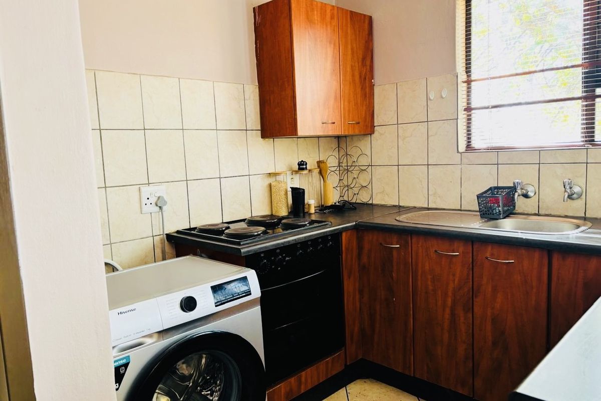 A functional kitchen featuring wood-tone cabinetry, tiled backsplash, integrated electric hob and oven, and a stainless steel sink with window view.