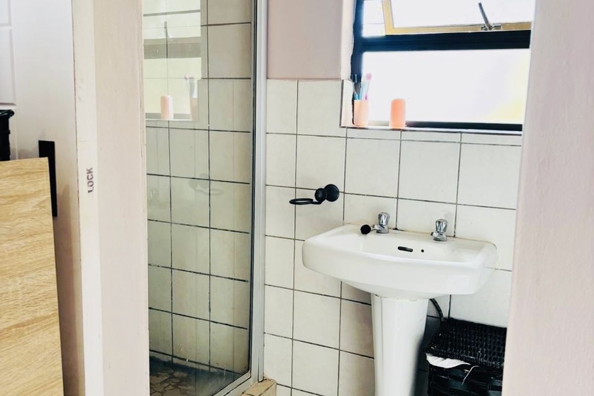 A functional bathroom featuring a pedestal basin, a glass-enclosed shower, and tiled finishes, offering a practical layout for daily use.