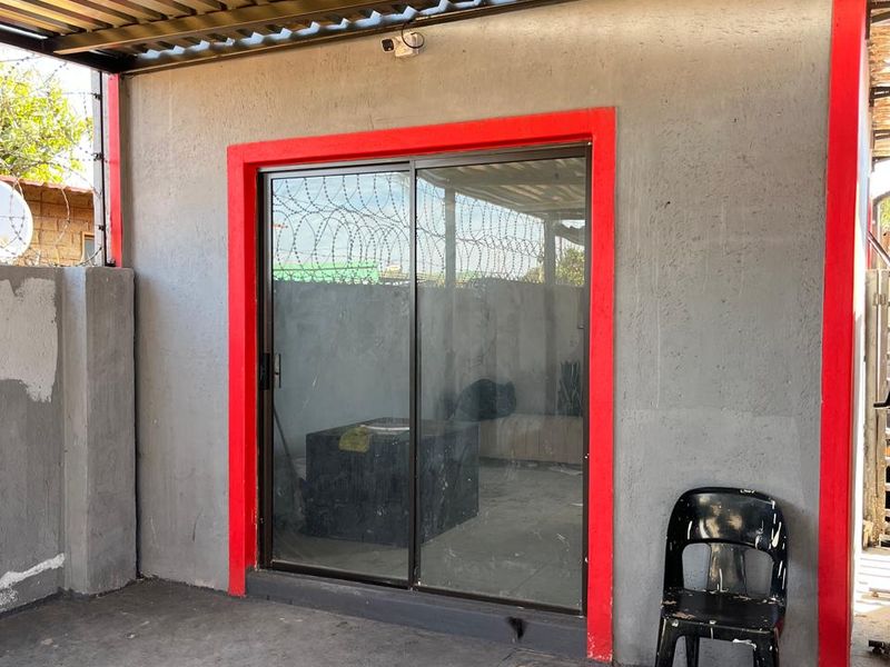 A covered outdoor patio area featuring a sliding glass door entrance, concrete flooring, and corrugated metal roofing.