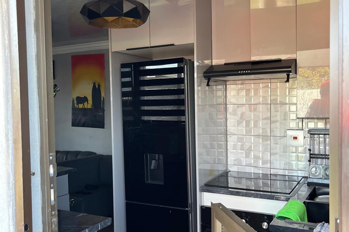 Compact modern kitchen featuring sleek cabinetry, a built-in hob with extractor fan, tiled backsplash, and stone countertops, viewed from an adjacent doorway.