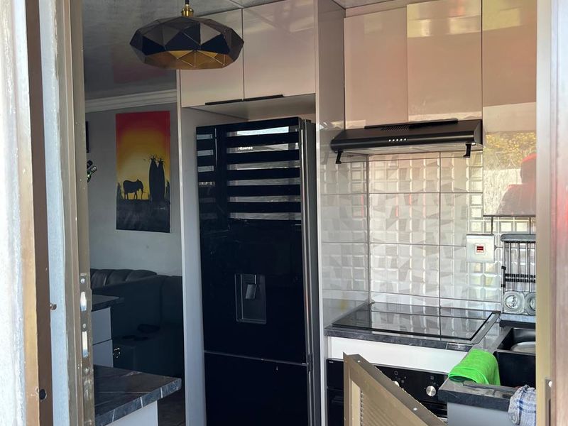 Compact modern kitchen featuring sleek cabinetry, a built-in hob with extractor fan, tiled backsplash, and stone countertops, viewed from an adjacent doorway.