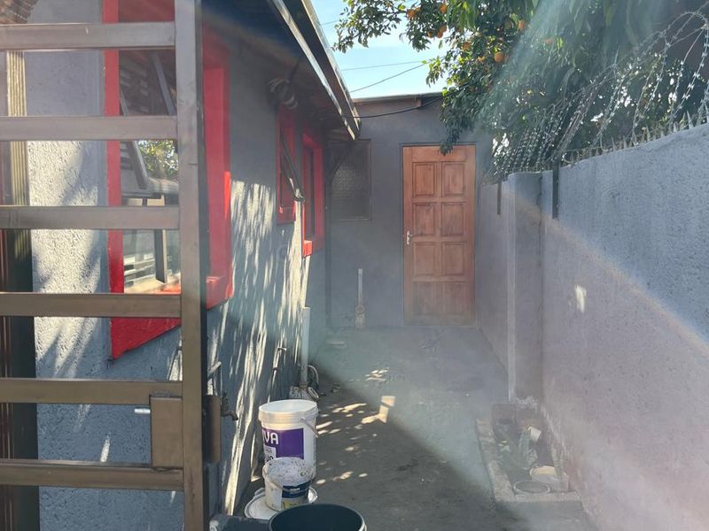 A narrow rear exterior walkway featuring a security gate, perimeter wall with barbed wire, and a timber door leading into the property.