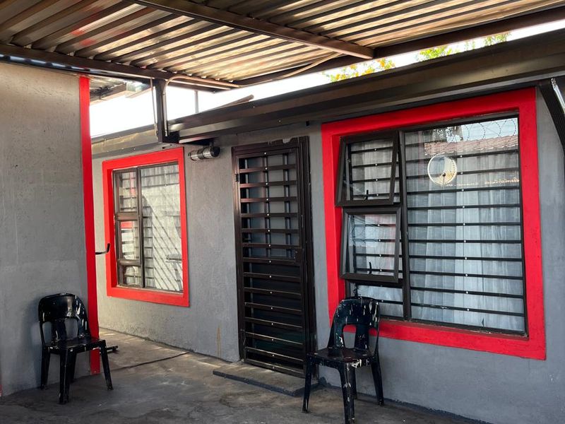 A covered outdoor patio area featuring a corrugated metal roof, security bars on windows, and a secure entrance gate.