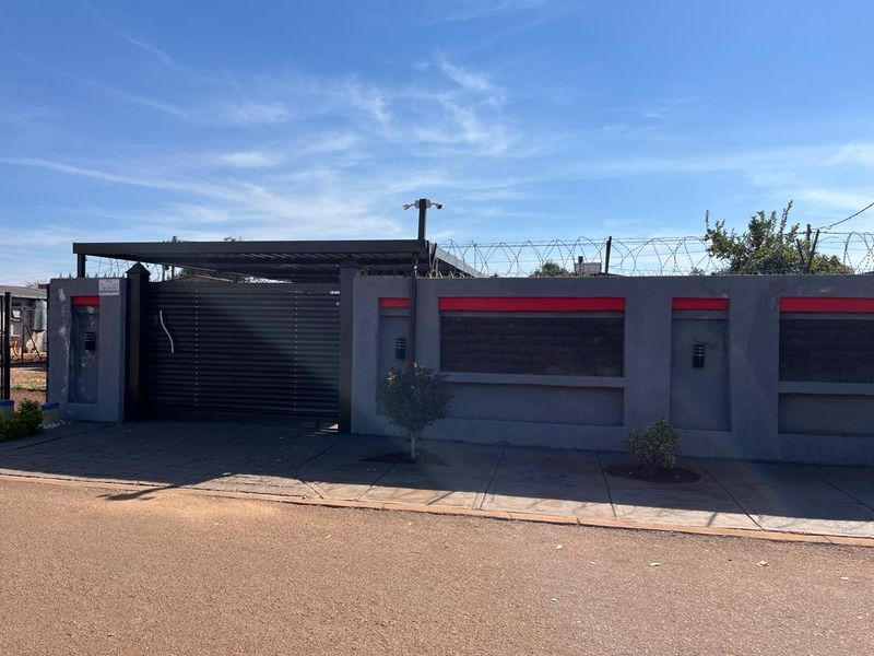 Front view of the property featuring a secure perimeter wall with razor wire, a modern sliding gate, and a covered carport area.