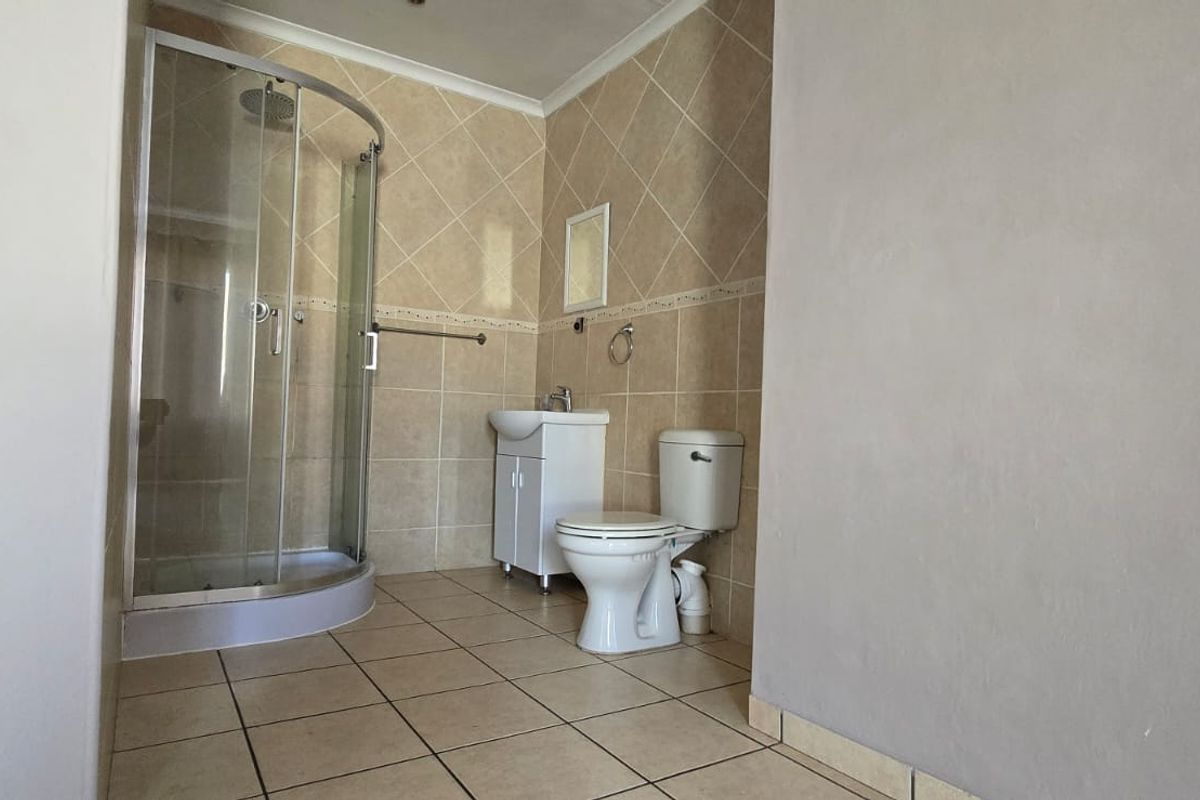 A functional bathroom featuring a corner shower enclosure, pedestal vanity, and ceramic toilet with neutral wall and floor tiling.